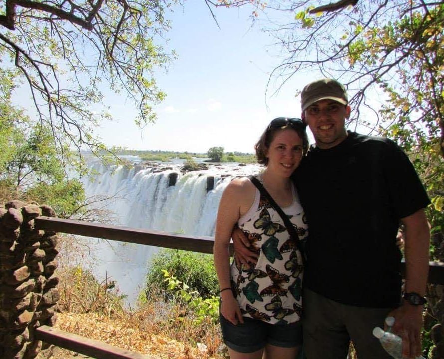 A man and woman pose for a photo while standing near a waterfall.