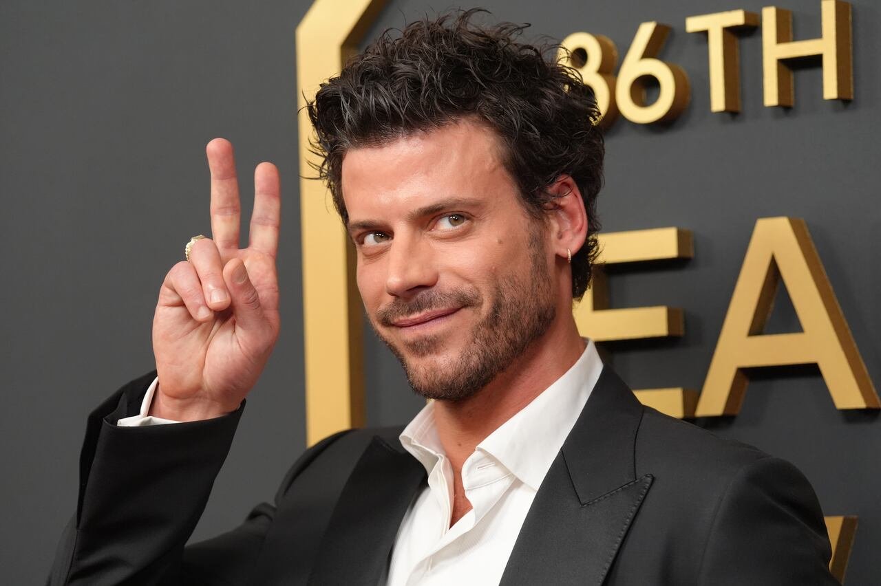 default-40 A man in a dark grey suit smiles and flashes a peace sign